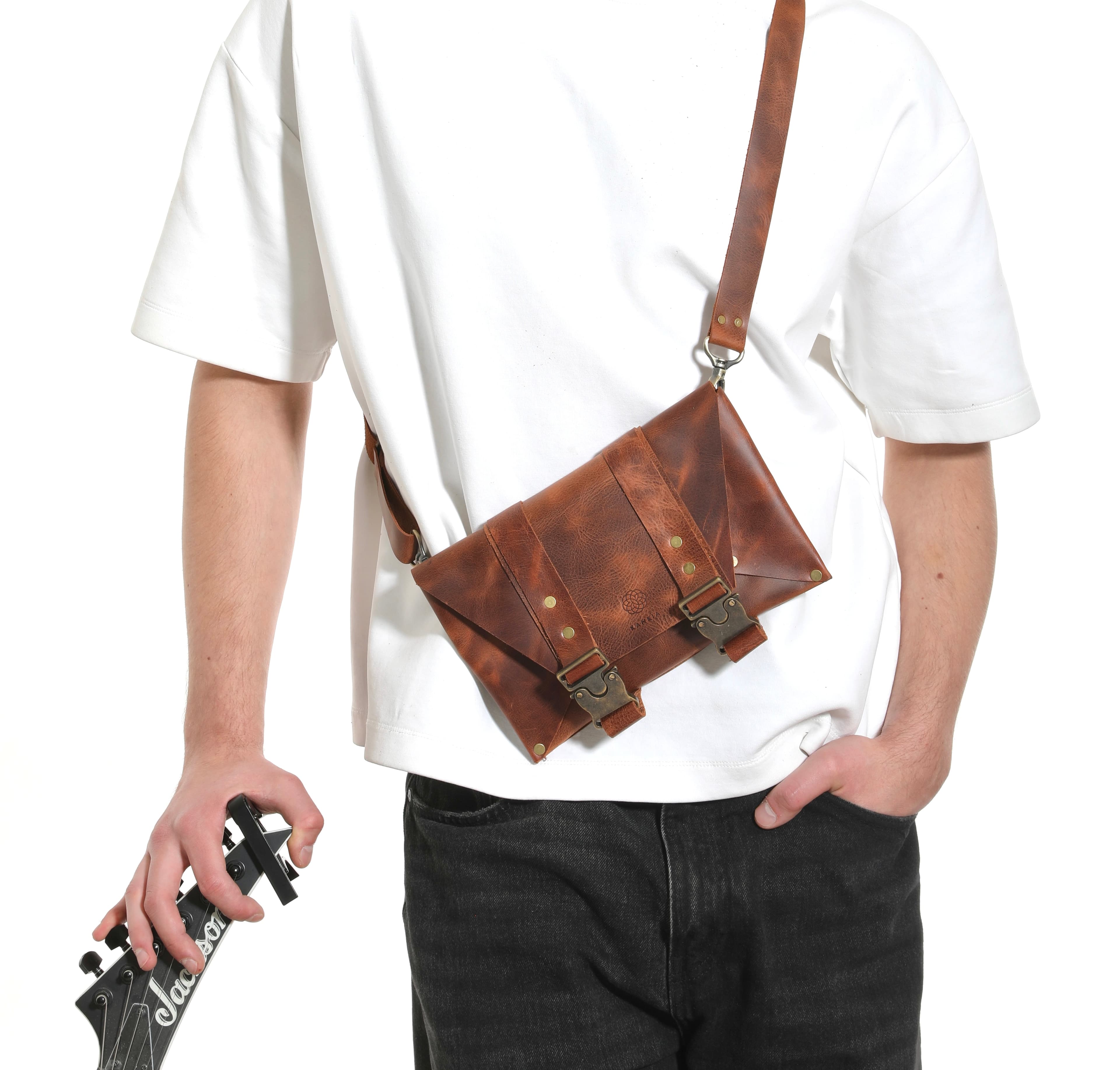 Model wearing a Kankia brown leather crossbody messenger bag, holding a guitar